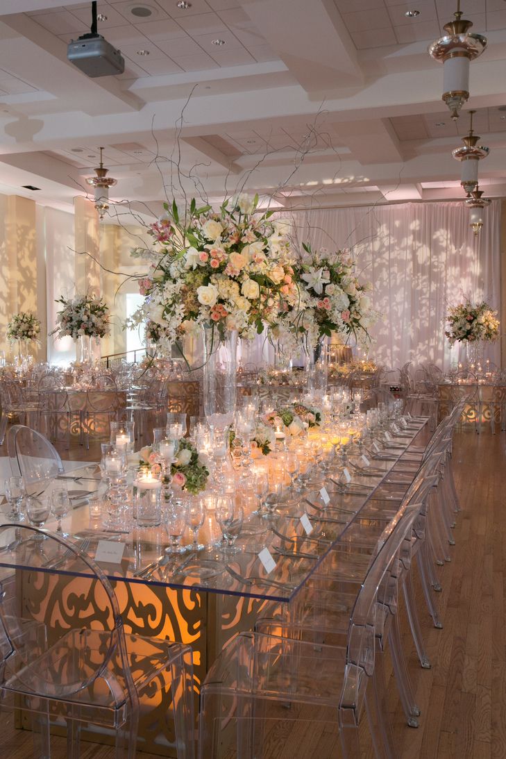 a long table is set up with clear chairs and centerpieces for an elegant event