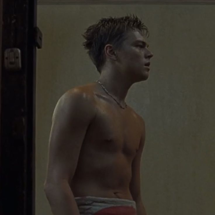 a shirtless young man standing in front of a mirror with his head turned to the side