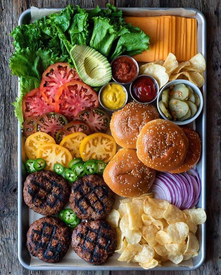 a tray filled with hamburgers, lettuce, tomatoes and other toppings