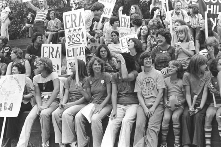 a group of people sitting on top of each other in front of a crowd holding signs