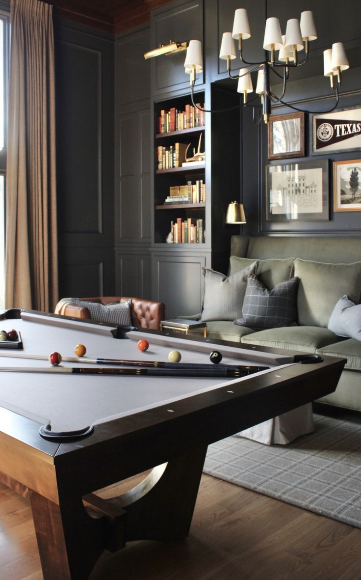 a pool table in the middle of a living room with couches and bookshelves