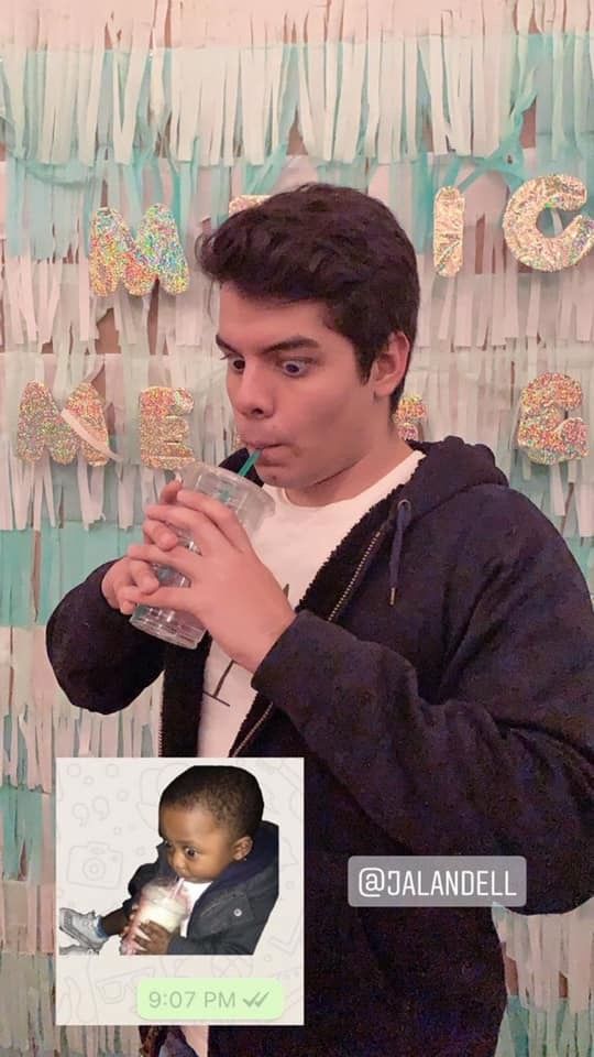 a young man drinking from a bottle while standing in front of a wall with decorations