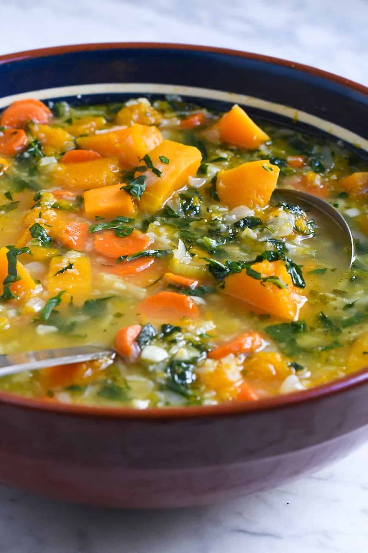 a bowl of soup with carrots, spinach and cheese in it on a table