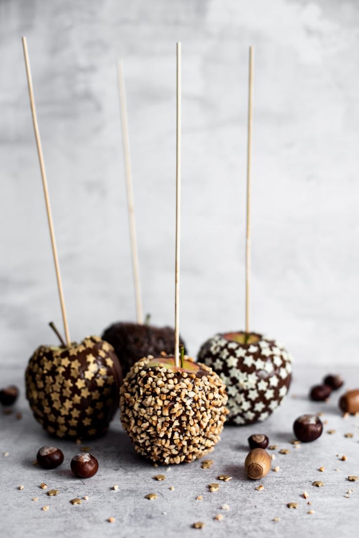 four chocolate covered apples with sprinkles and nuts scattered around them on a table