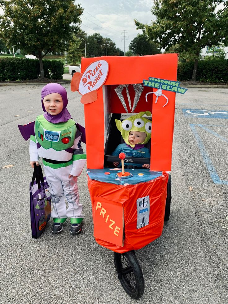 two children dressed up as toy story book characters in front of an orange box cart