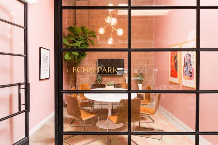 an office with pink walls and glass doors that lead into the dining room area, where there is a small round table surrounded by brown chairs