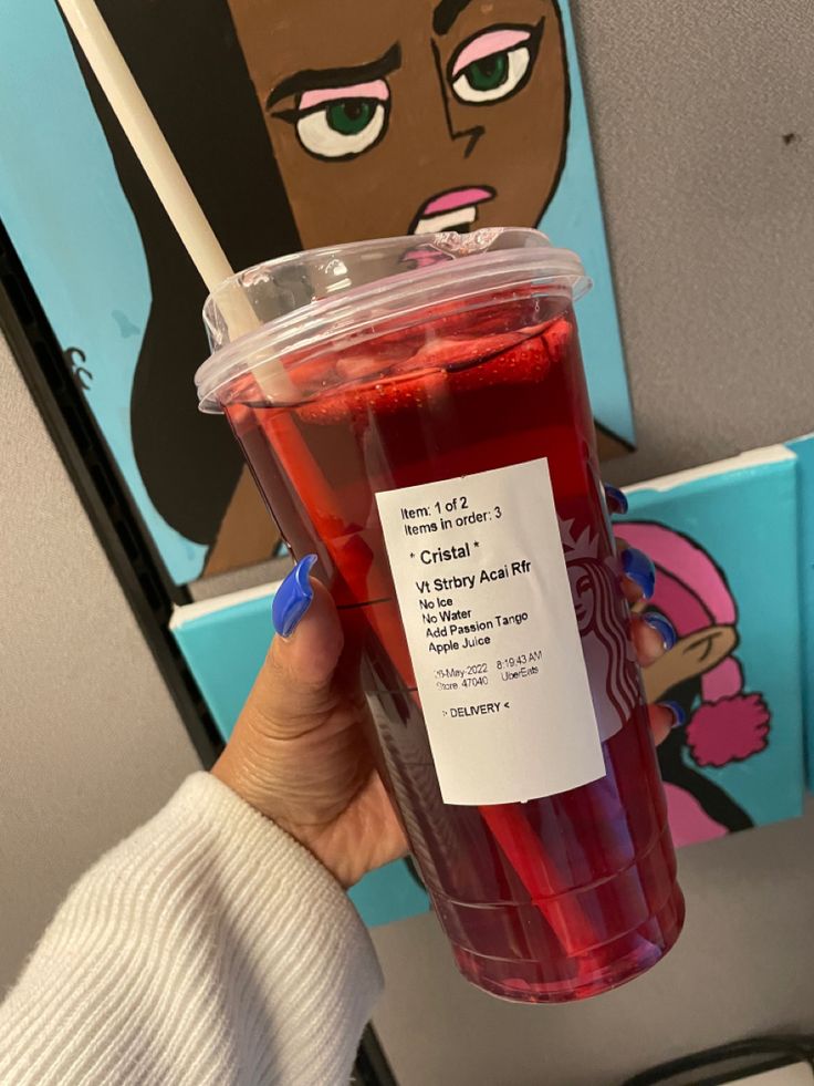 a person holding up a cup with red liquid in it and a sticker on the lid