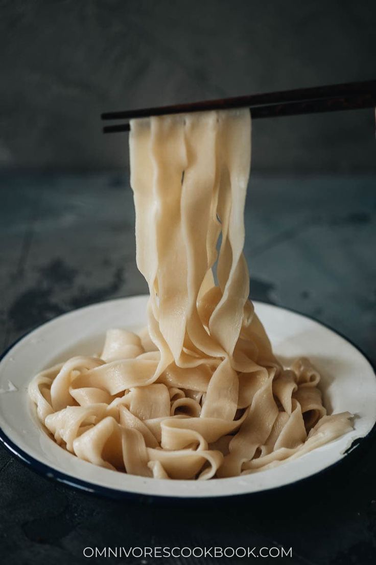 noodles being lifted by chopsticks from a white plate with black trim on it