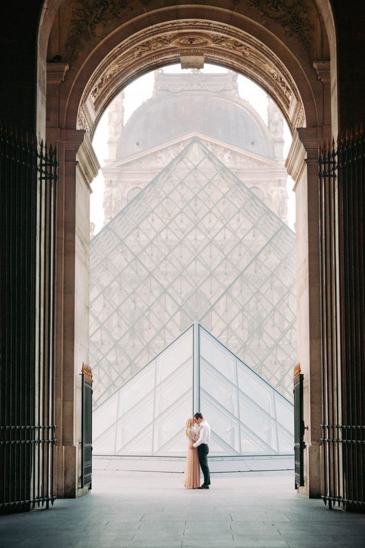 an engaged couple standing in front of the pyramid at the musee de l'eiffel