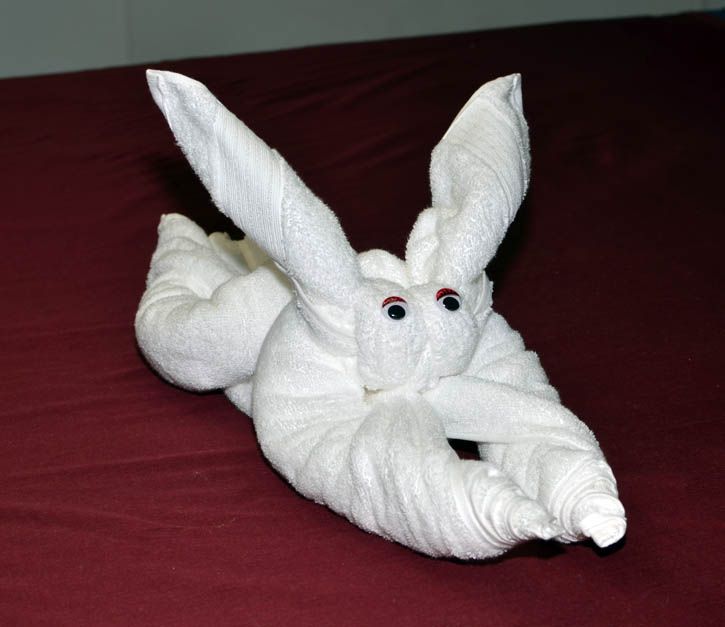 an elephant made out of towels sitting on top of a red bed spread with its trunk stretched out