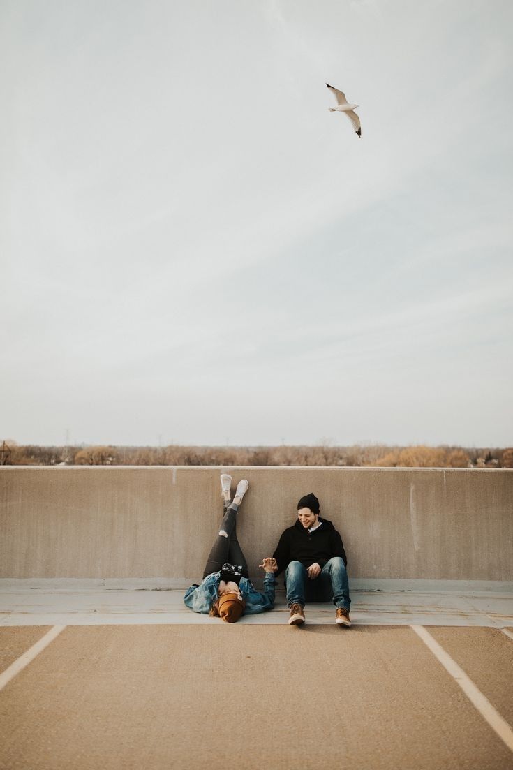 two people sitting on the ground with a bird flying overhead