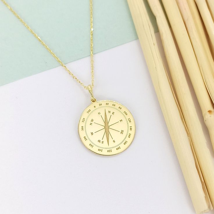 a gold compass necklace sitting on top of a white table next to sticks and straws