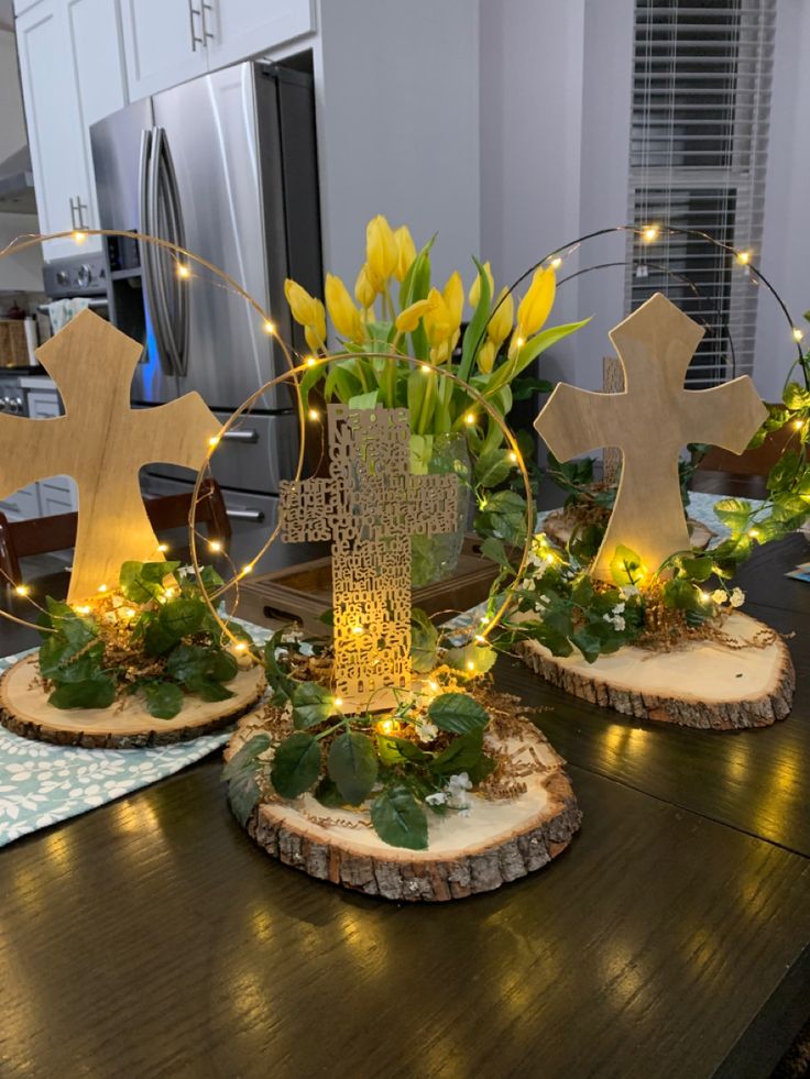 two wooden crosses are decorated with lights and greenery on top of the wood slices