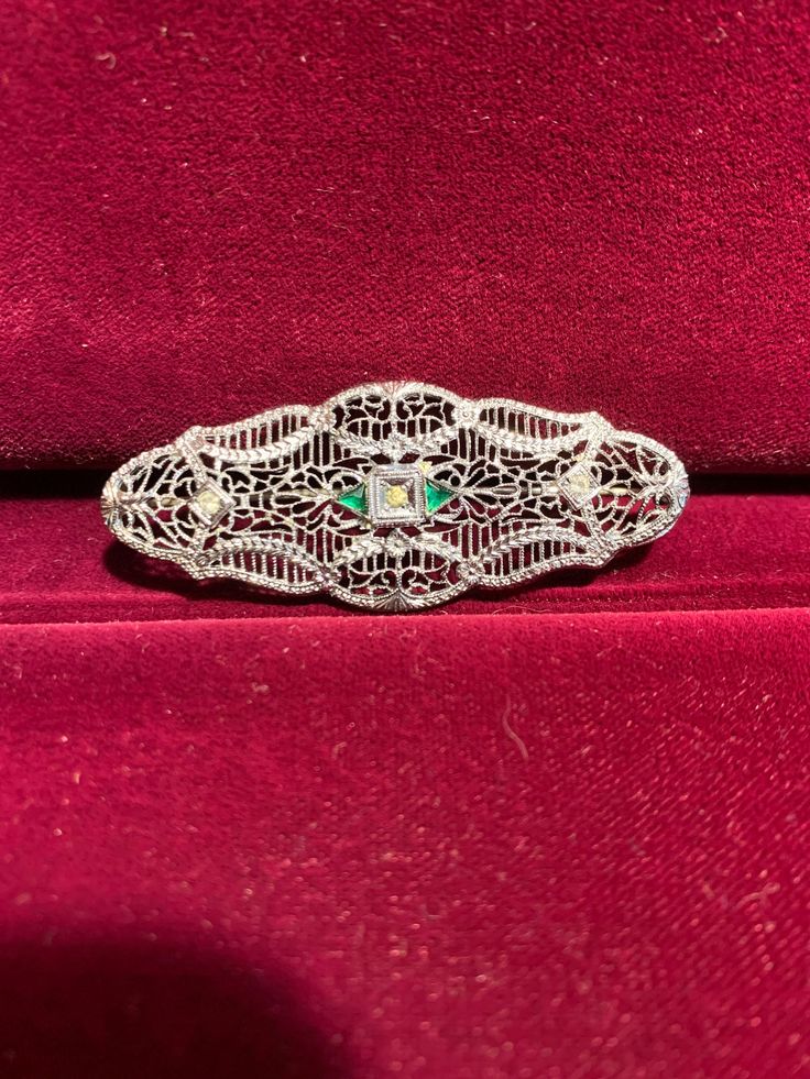 Excellent representation of a classic Victorian Filigree pin in Sterling Silver with white and green synthetic accent stones, which mimic diamond and emerald brooches from that period. This piece from our Estate Collection is in excellent condition. The pin stem is held in place via a safety clasp. This piece may be worn horizontally, vertically, or even on the diagonal, as you wish. It could even be worn vertically on a chain, if desired. While this piece is vintage, it is not technically an antique; although only you need to know as this will easily pass as a well-preserved antique. Elegant Green Diamond Brooch, Vintage Green Diamond Brooches, Green Diamond Wedding Brooches, Formal Diamond Filigree Brooches, Elegant Green Oval Brooches, Ornate Diamond Brooches For Formal Occasions, Ornate Diamond Brooch For Formal Wear, Ornate Diamond Brooch For Formal Occasions, Formal Silver Jeweled Brooches