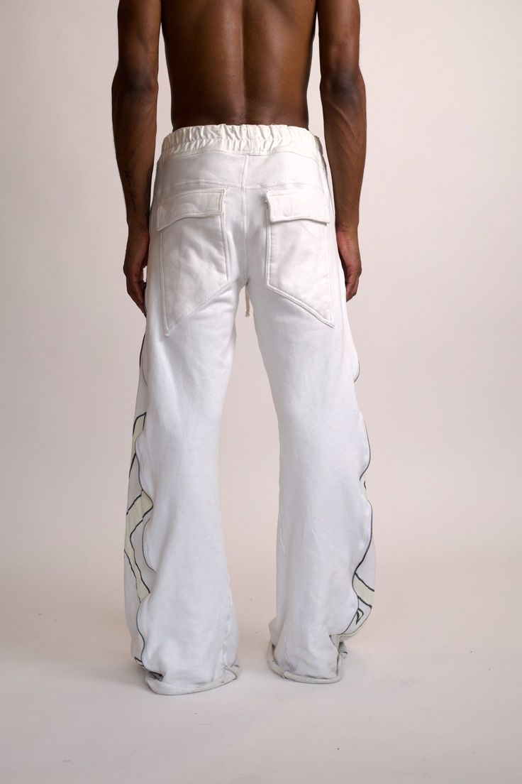 STERRE PEYTON CYBERIA CONTRA FLARED SWEAT PART OF THE NU SZN COLLECTION. THIS PANT INCLUDES A DRAWSTRING WAISTBAND AND A BUTTON FLY. THIS PANT INCLUDES FOUR POCKETS. THIS PANT FEATURES LONG ZIPPERS ON BOTH SIDES WHICH CAN BE OPENED AND ADJUSTED TO EXPOSE THE FLARED PANELS. EACH PANEL FEATURES THE SIGNATURE CONTRA DESIGN. THESE PANTS ARE MADE OUT OF A HEAVYWEIGHT COTTON JERSEY FOR WARMTH AND COMFORTABILITY. COLORS: White, Cream, Black This garment is a hand painted piece. Paint marks are to be ex Urban White Pants For Streetwear, Urban White Streetwear Pants, White Urban Style Pants For Streetwear, Urban White Cotton Bottoms, Urban Style White Cotton Bottoms, White Streetwear Pants With Side Pockets, White Straight Leg Bottoms For Streetwear, White Baggy Parachute Pants For Loungewear, Urban White Bottoms For Spring