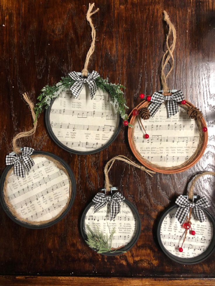 four christmas ornaments hanging on a wooden table with sheet music and greenery around them