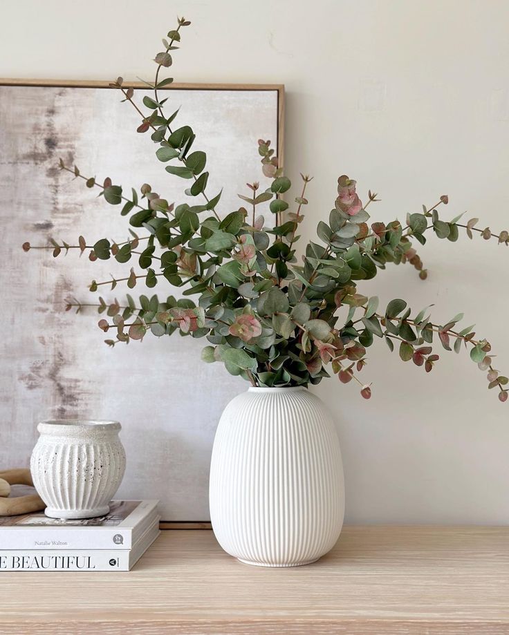 there is a vase with flowers in it next to a stack of books on the table