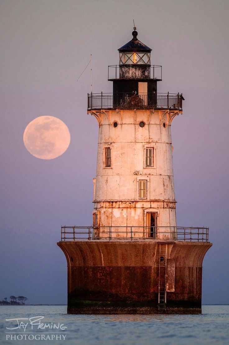 the full moon is setting behind a lighthouse