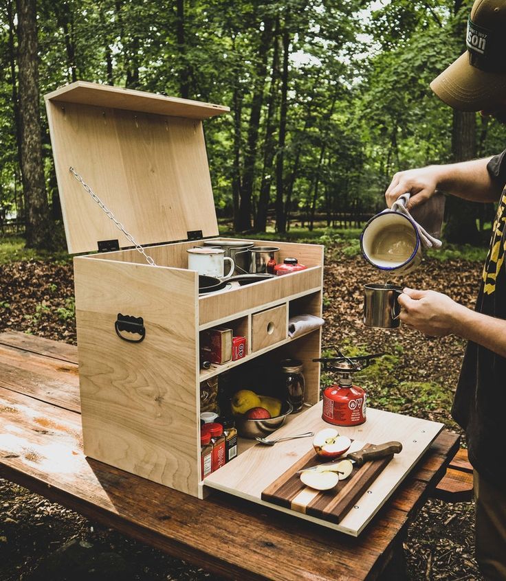 a man is holding a cup near an open box on a picnic table in the woods