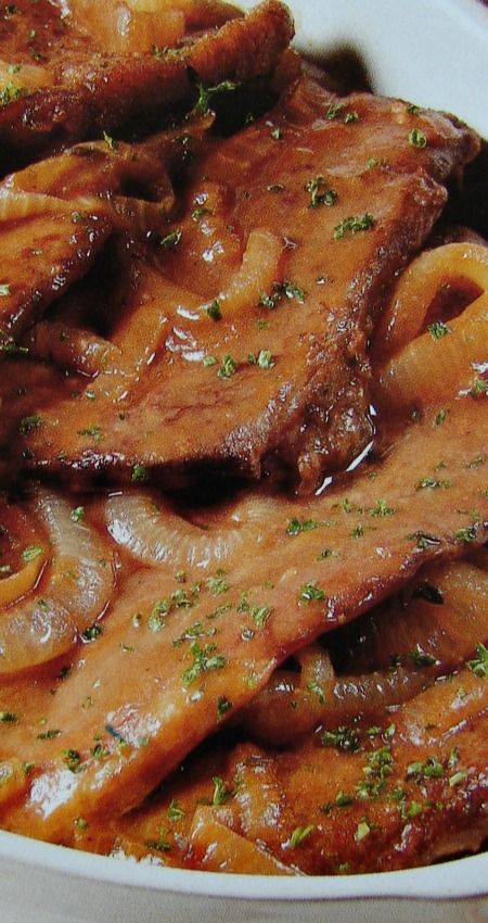 a white bowl filled with meat covered in gravy on top of a table