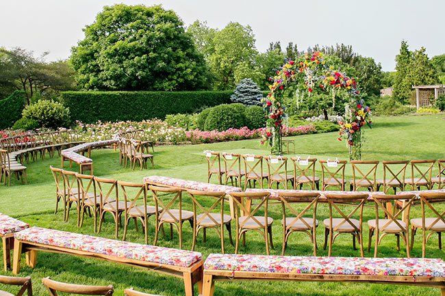 an outdoor ceremony setup with wooden chairs and floral arrangements on the lawn, surrounded by lush greenery