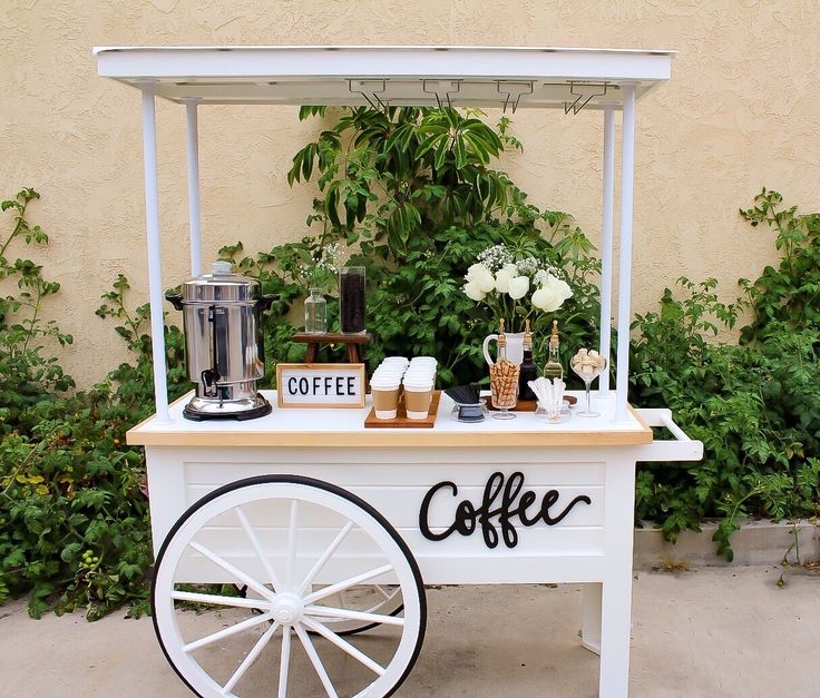 an outdoor coffee cart is set up with flowers and greenery on the sidelines