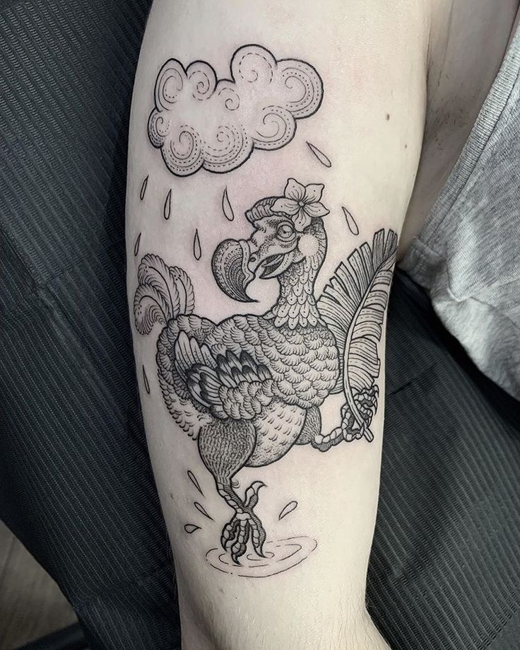 a black and white tattoo of a rooster on the left arm with clouds in the background