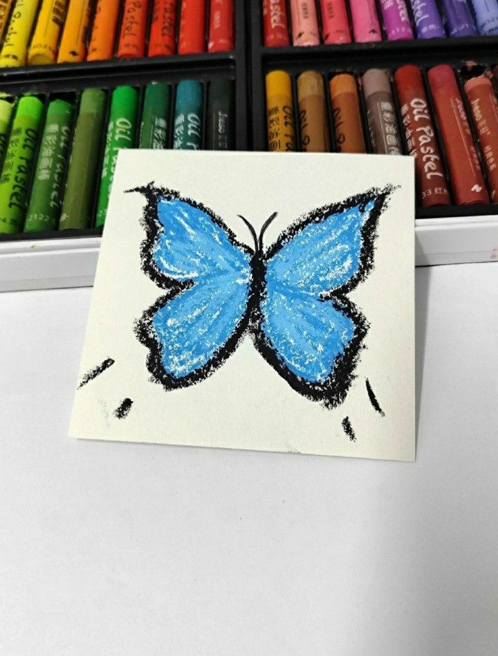 a drawing of a blue butterfly with crayons in the background