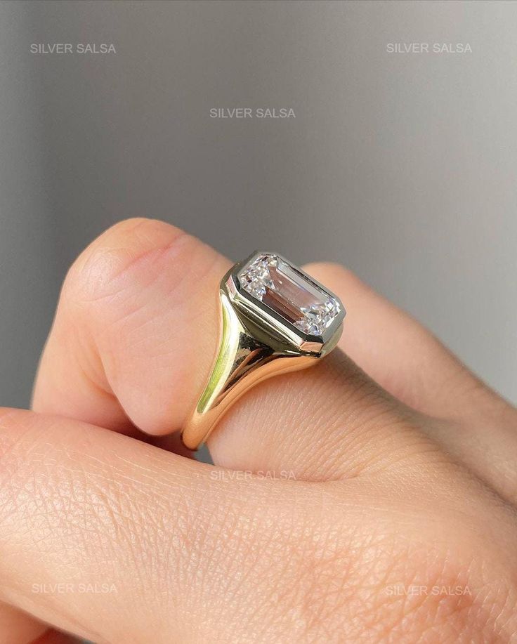 a woman's hand holding a ring with a diamond on it and the middle finger