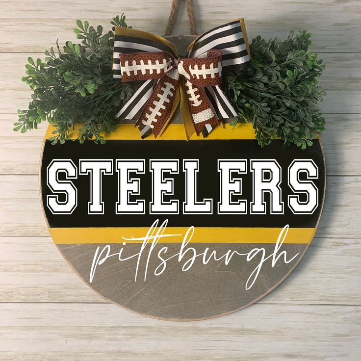 a pittsburgh football sign hanging on the side of a wooden wall with greenery around it