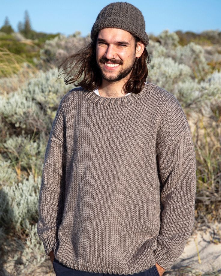 a man with long hair wearing a brown sweater and beanie smiles at the camera