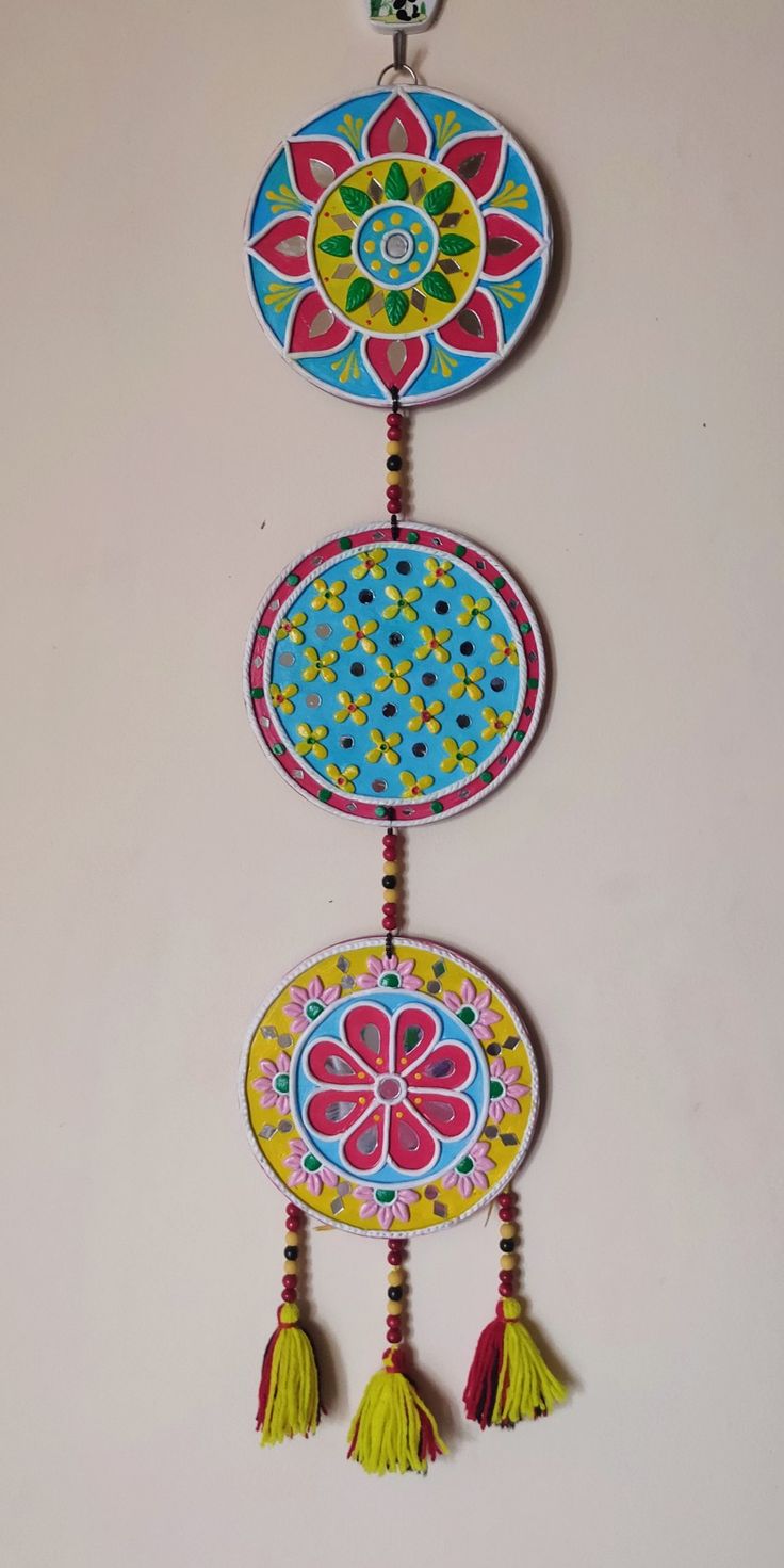 three colorful plates with tassels hanging from the side on a white wall,