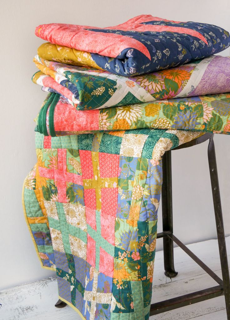 three quilts stacked on top of each other near a bar stool with a metal frame