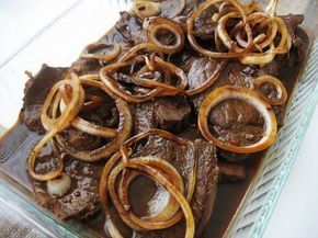 beef and onions in a glass dish with brown sauce on the side, ready to be eaten