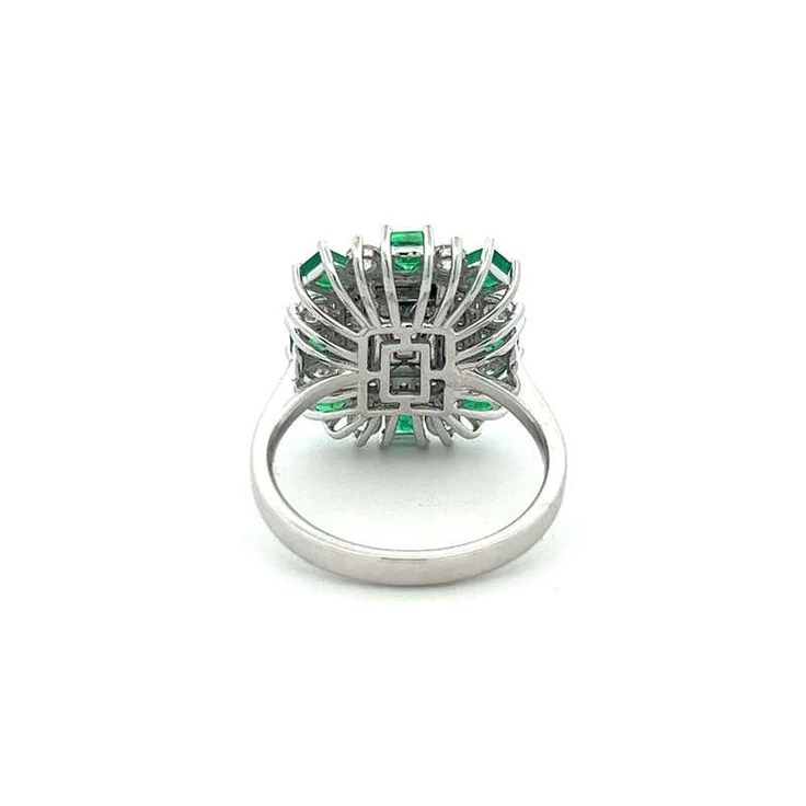 an emerald and diamond ring, with the center stone surrounded by smaller stones in white gold