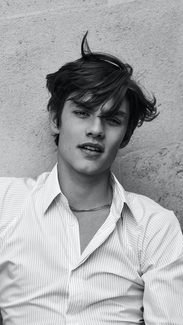 black and white photograph of a young man with his hair blowing in the wind, leaning against a wall