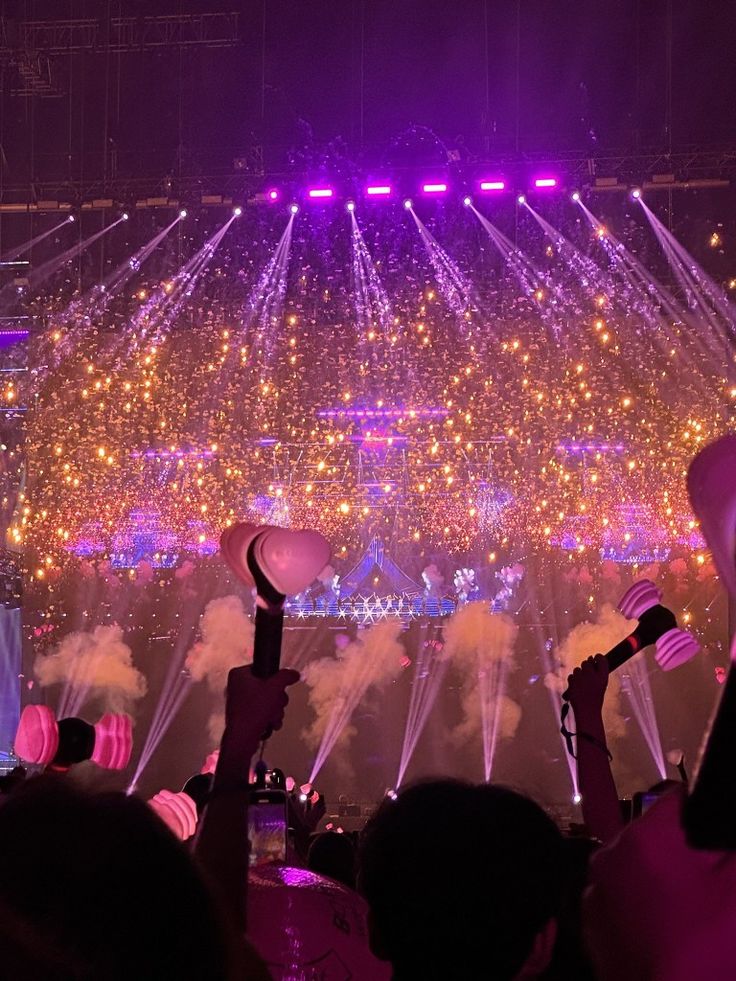 fireworks are lit up in the night sky as people watch from their seats at a concert