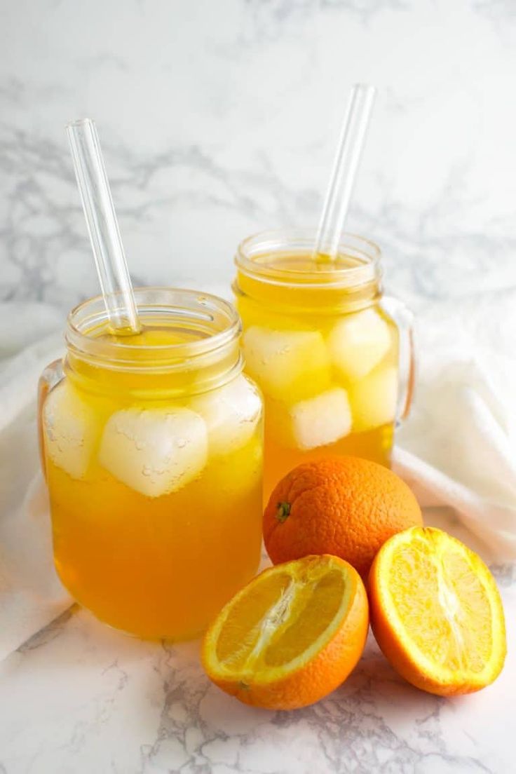 two mason jars filled with lemonade and oranges next to each other on a marble surface