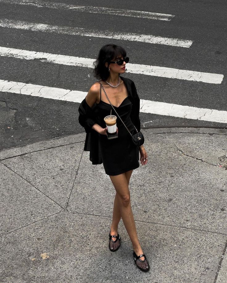 a woman is standing on the sidewalk with a cup of coffee