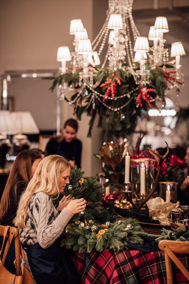 a woman sitting at a table in front of a chandelier with christmas decorations