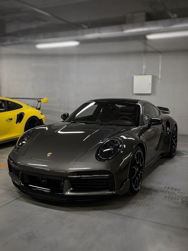 two sports cars parked in a garage next to each other, one yellow and the other black