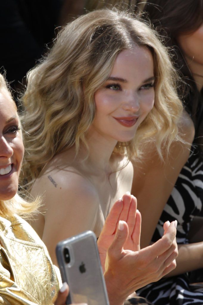 two women sitting next to each other in front of a crowd, one holding a cell phone