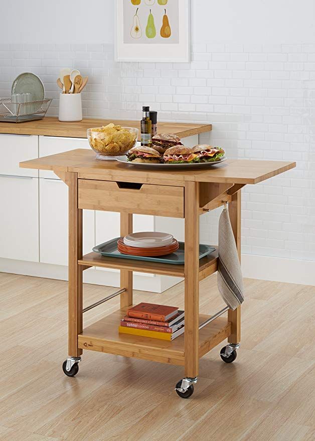 a kitchen cart with food on it in front of a white wall and wooden floors