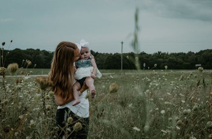 a woman holding a baby in her arms while standing in the middle of a field