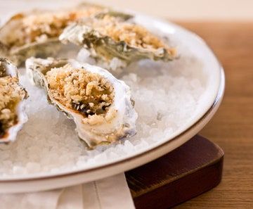 oysters on ice with crumbs and seasoning sitting on a white plate