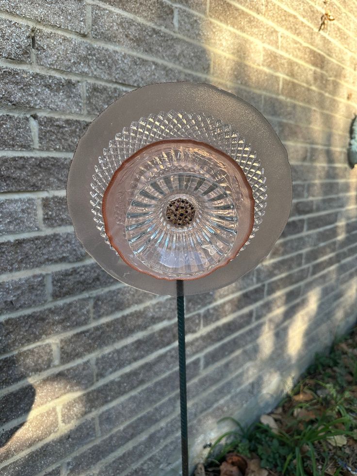 a glass flower on a metal stand in front of a brick wall and green grass