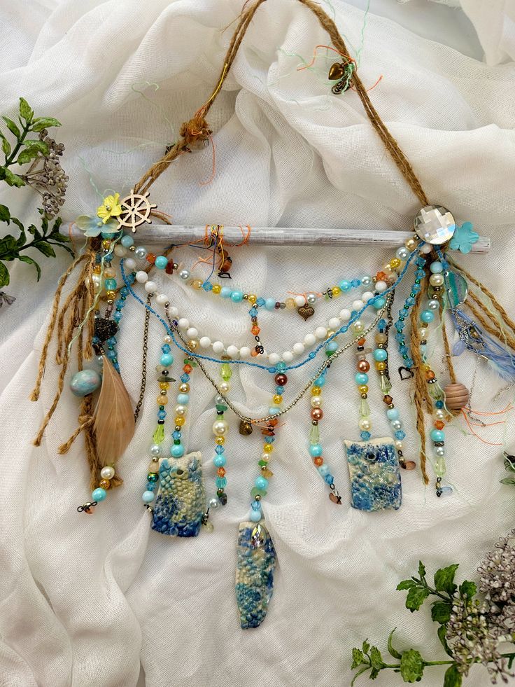 a piece of art with beads and feathers hanging from it's side on a white cloth