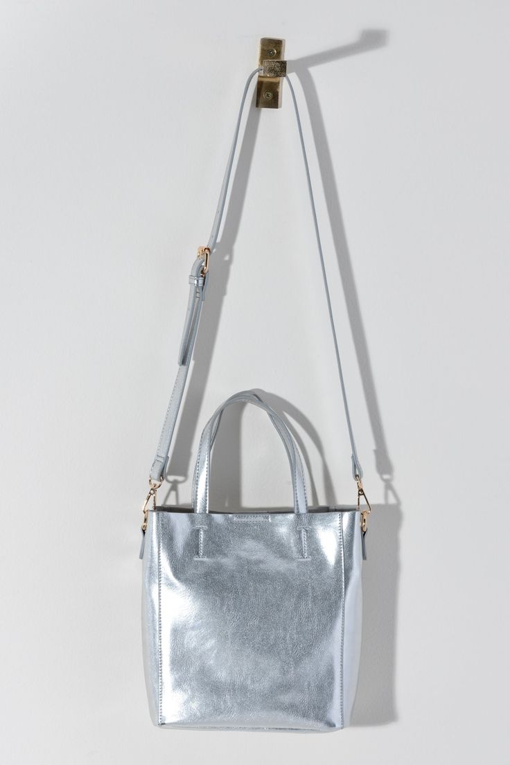 Make a statement this summer with Shiraleah's Maddie Mini Tote. Made from metallic PU, this shiny accessory is sure to turn heads. Add some versatility to your style by wearing with the detachable adjustable cross-body strap or carry with the standard double handles. Pair with other Shiraleah items to complete your look! Features double handles, a detachable adjustable cross-body strap, magnetic snap closure, and 1 inner slip pocket Shiraleah is a trend-driven lifestyle brand focused on the litt Purse Scarf, Blue Springs, Hair Accessories Jewelry, Accessories Jewelry Necklace, Mini Tote, Love Is Free, Sunglasses Sale, Lifestyle Brand, Slip On Sneakers