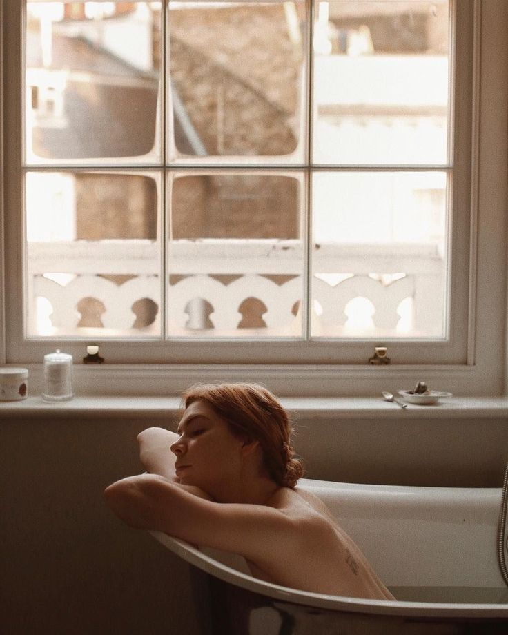 a woman laying in a bathtub next to a window