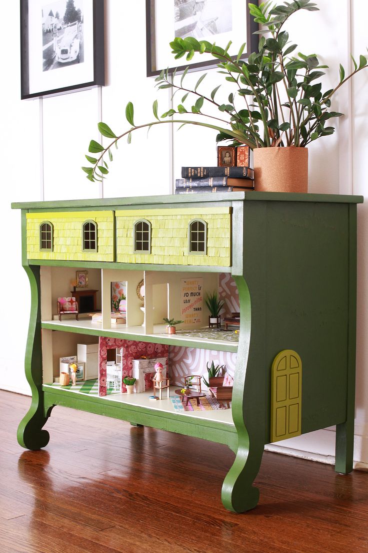 a toy house on top of a book shelf with plants in the corner next to it